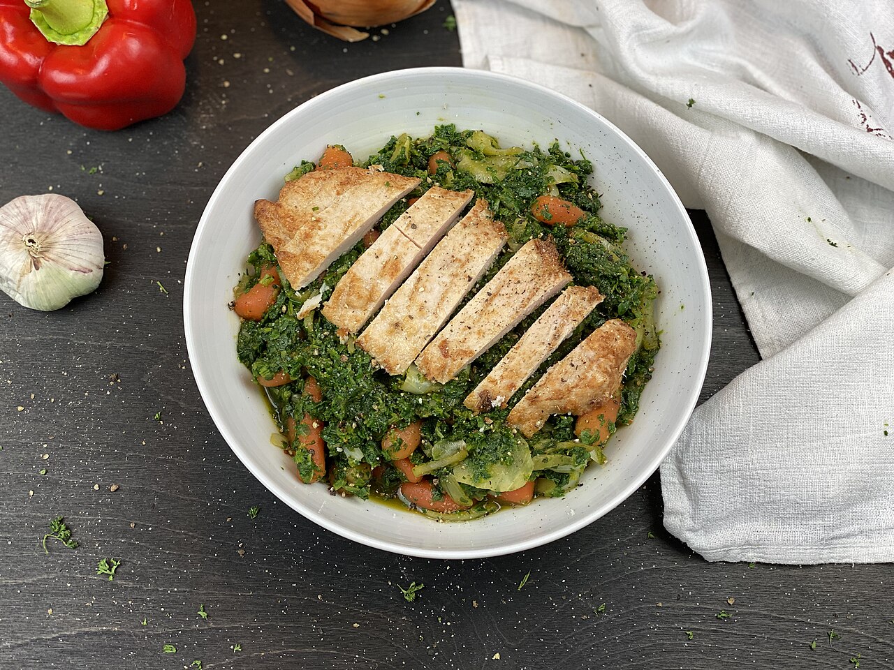 Prato de frango grelhado sobre espinafre e legumes, sem arroz, pão ou massa visíveis.